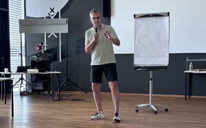 Knut Kircher während seines Vortrags beim Begegnungswochenende der Sehhunde. Er hält ein Mikrofon in der Hand und steht vor einem Whiteboard.